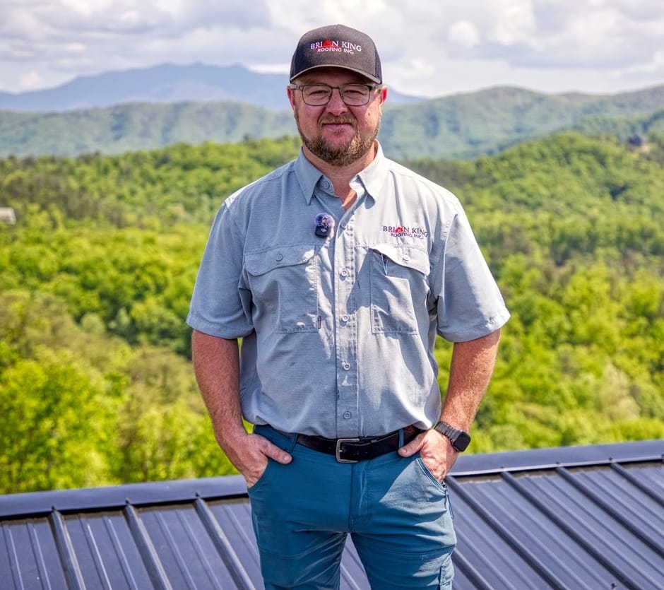 Ryan King standing on a standing seam metal roof with the Great Smoky Mountains behind him